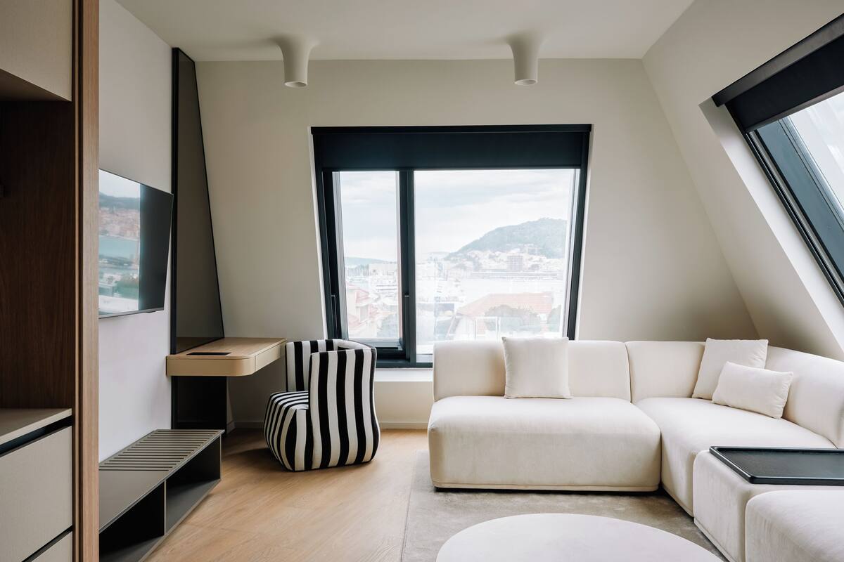 Una sala de estar moderna con un sofá, un sillón a rayas, un televisor y un ventanal con vistas a la ciudad.