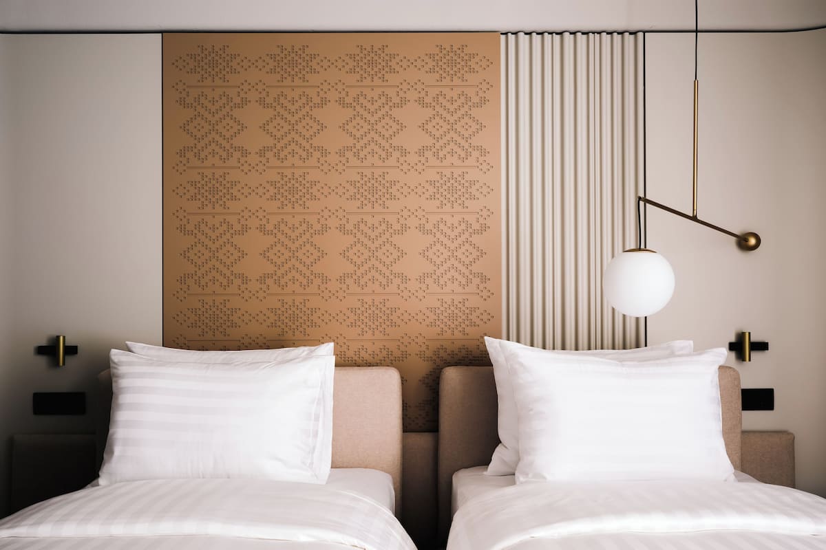Habitación de hotel con dos camas, un cabecero estampado, una lámpara colgante y una mesita de noche.