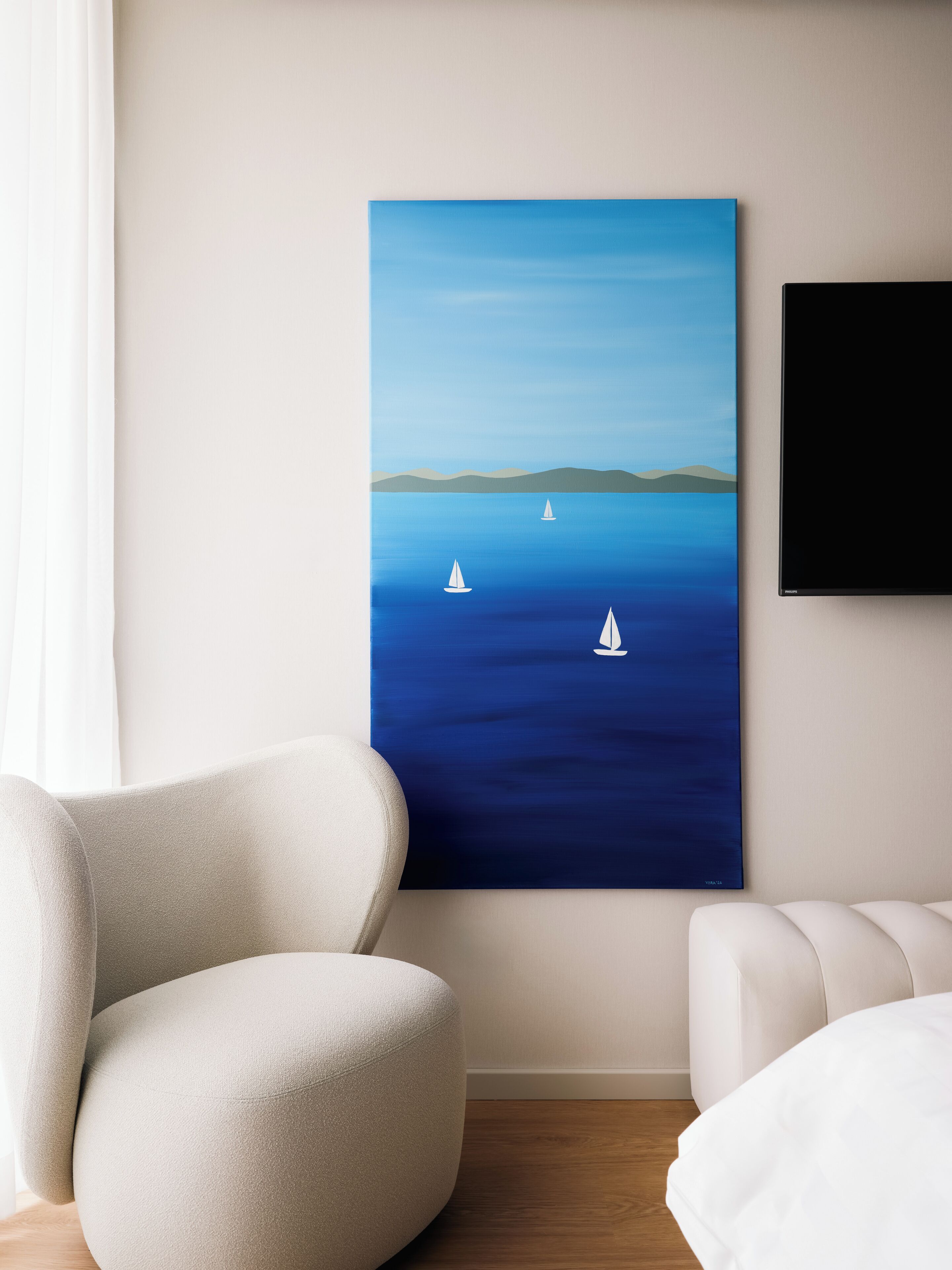 Een kamer met een groot schilderij van een rustige zee en zeilboten, een witte fauteuil en een wandtelevisie.