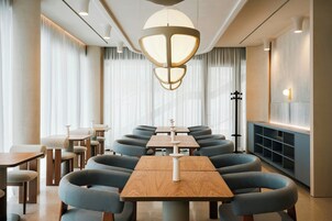 Et moderne spiseområde med runde borde og stole, en centralt placeret lampe og en hylde på væggen.