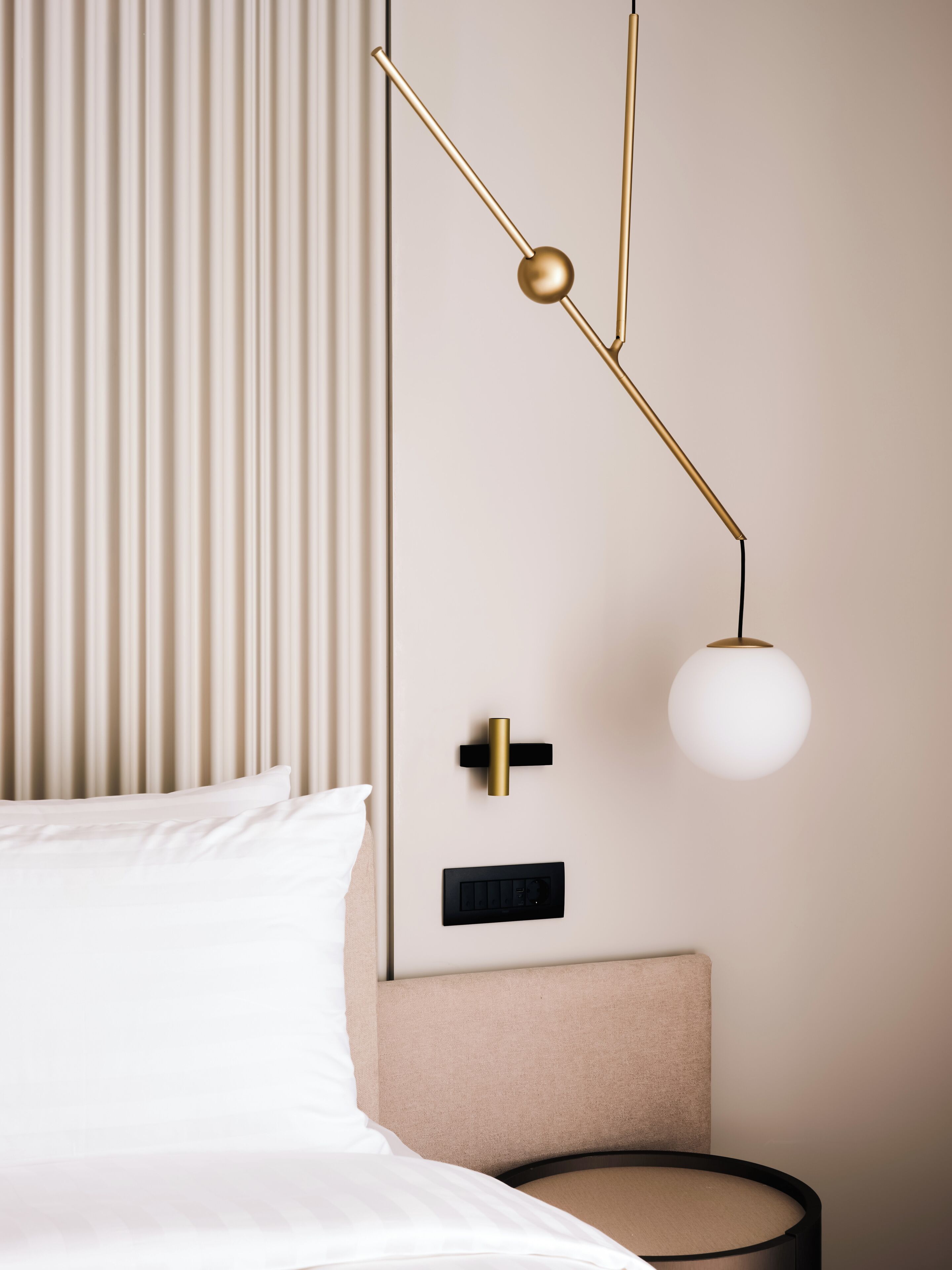 A bed with white linens, a bedside table with a lamp, and a wall-mounted control panel.