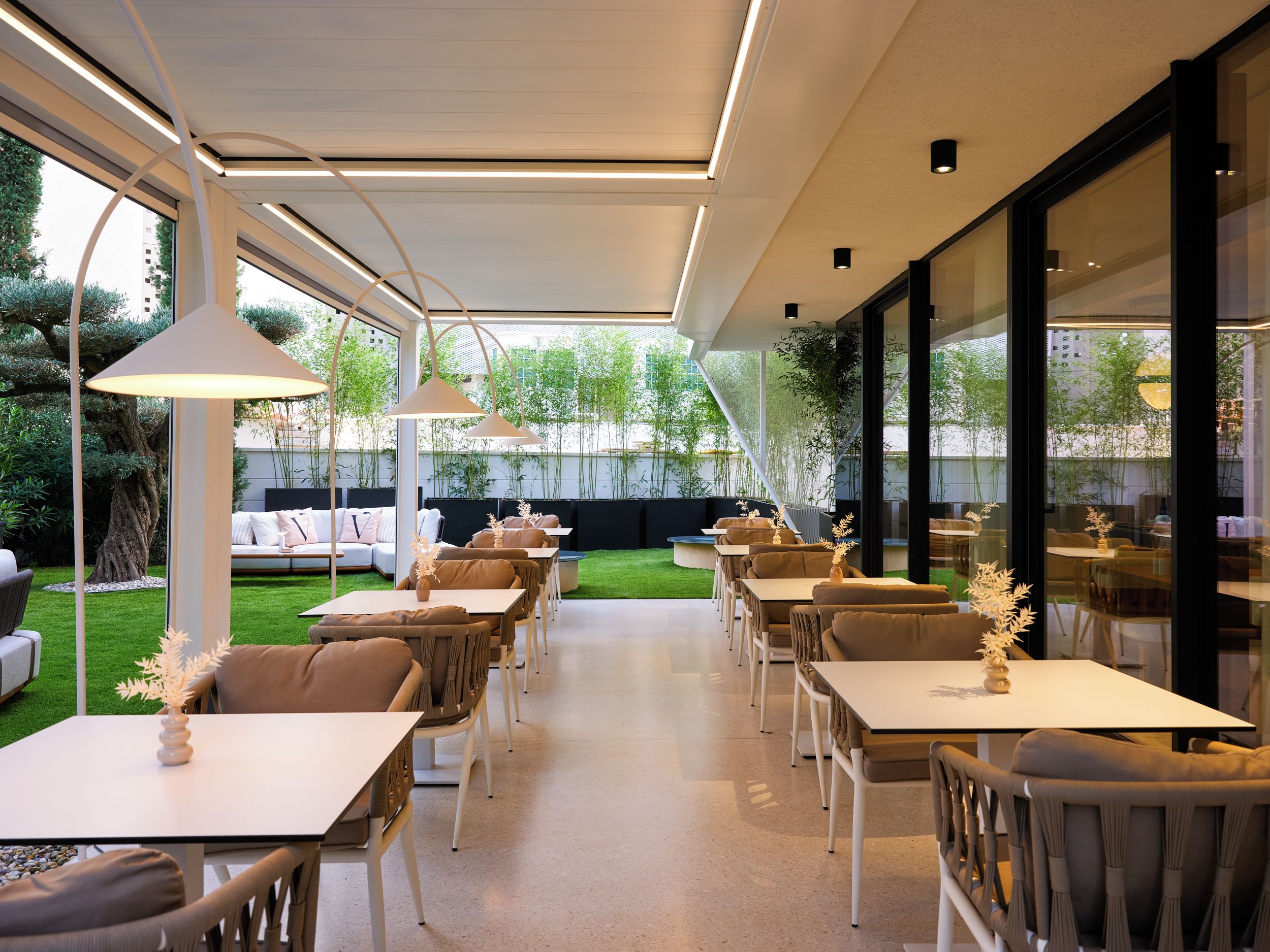 Un patio al aire libre con mesas, sillas y un sofá, junto a un árbol grande.