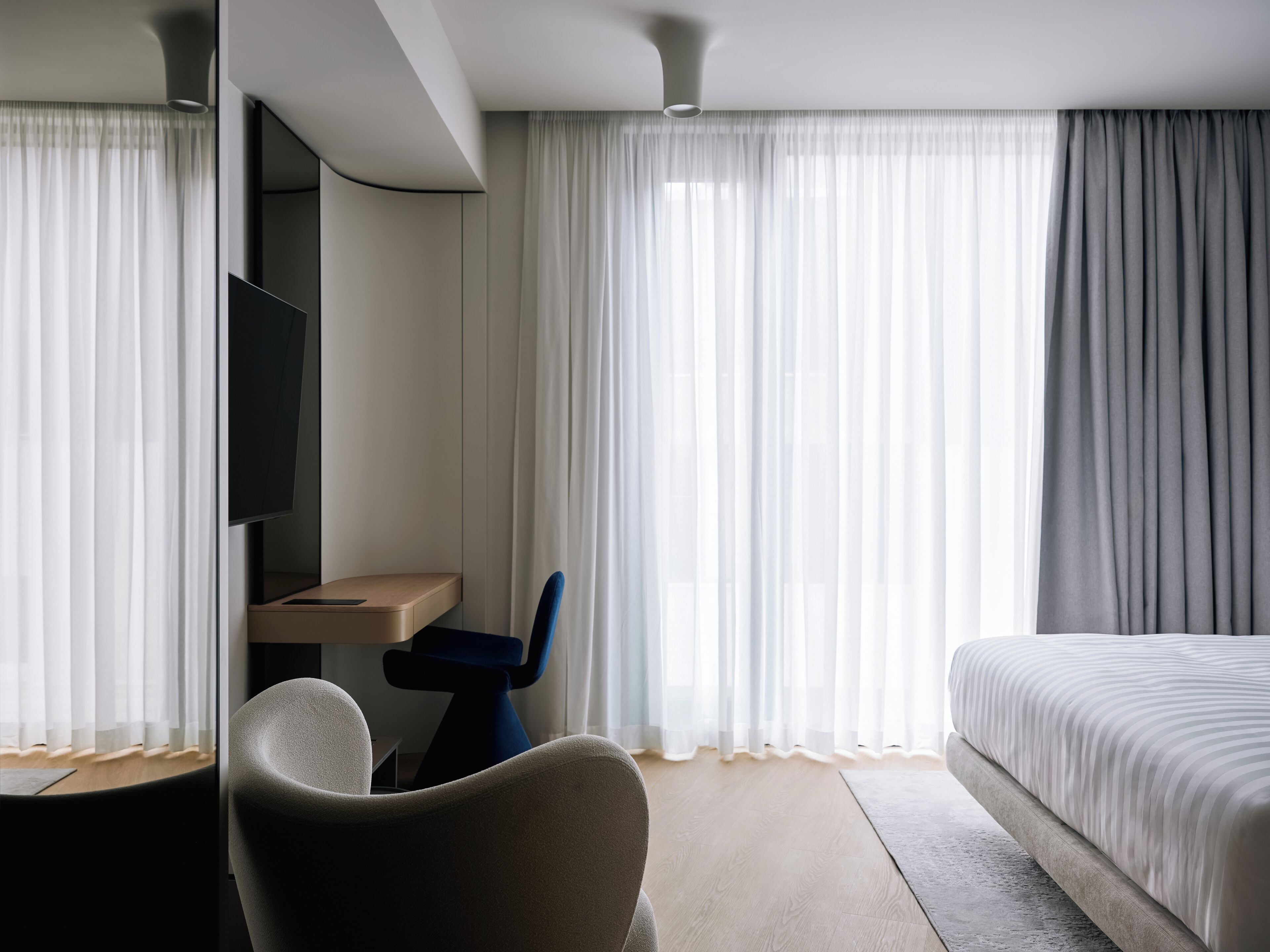A modern hotel room with a bed, a desk, a chair, and a TV.