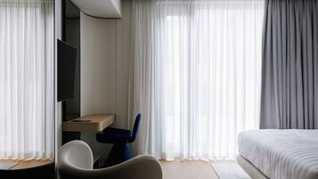 A modern hotel room with a bed, a desk, a chair, and a TV.