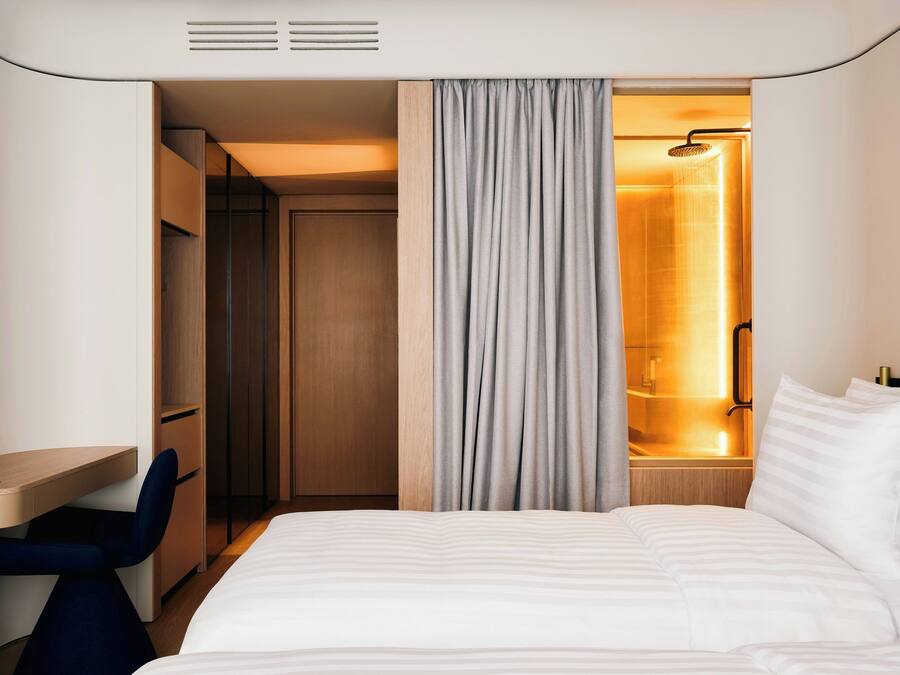 A hotel room with a bed, a desk, a chair, a wardrobe, and a shower area.