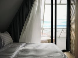Et soveværelse med seng, udsigt til stranden og en skydedør.