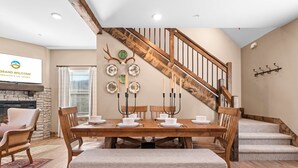 A dining area with a wooden table set for four, surrounded by chairs, a bench, and a staircase with a wooden railing.