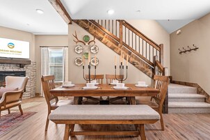 A dining area with a wooden table set for four, surrounded by chairs, a bench, and a staircase with a wooden railing.