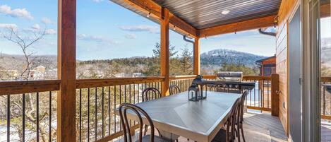 A covered outdoor dining area with a table and chairs, overlooking a mountainous landscape.
