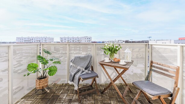A balcony with a wooden floor, a chair, a table with a plant, and a view of buildings in the background. - Lumina 3-rooms apart with balcony (Łódź)