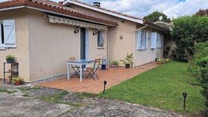 A two-story house with a tiled roof, a front porch with a table and chairs, and a small garden area. - QUIRI45-40000 (Mont-de-Marsan)