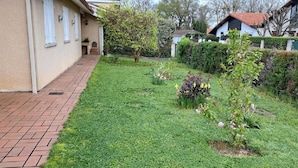 A residential garden with a paved walkway, various flowering plants, and a house with a tiled roof. - QUIRI45-40000 (Mont-de-Marsan)