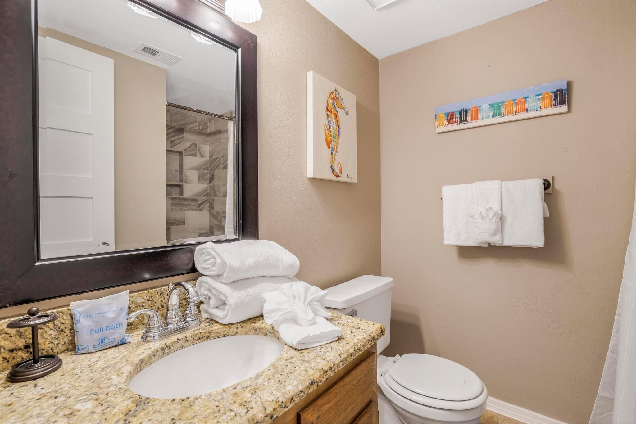 A bathroom with a granite countertop sink, a white toilet, a towel rack, and a mirror with a wooden frame.