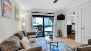 Ein Wohnzimmer mit einer Couch, einem Couchtisch und Blick auf einen Balkon mit einem Sessel.