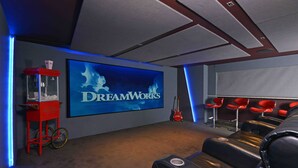 Ein Heimkinozimmer mit einer großen Leinwand, die 'DreamWorks' zeigt, einem roten Lautsprecherwagen, einer roten E-Gitarre und einer Reihe roter Sessel.