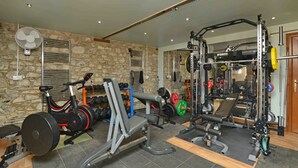 Ein Heimfitnessraum mit unterschiedlichen Trainingsgeräten, darunter ein Laufband, eine Gewichtbank und ein Squat-Stand.