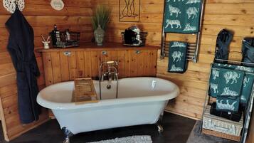 A bathroom with a freestanding bathtub, wooden walls, a towel rack with tiger-patterned towels, a small shelf with toiletries, and a decorative Buddha head.