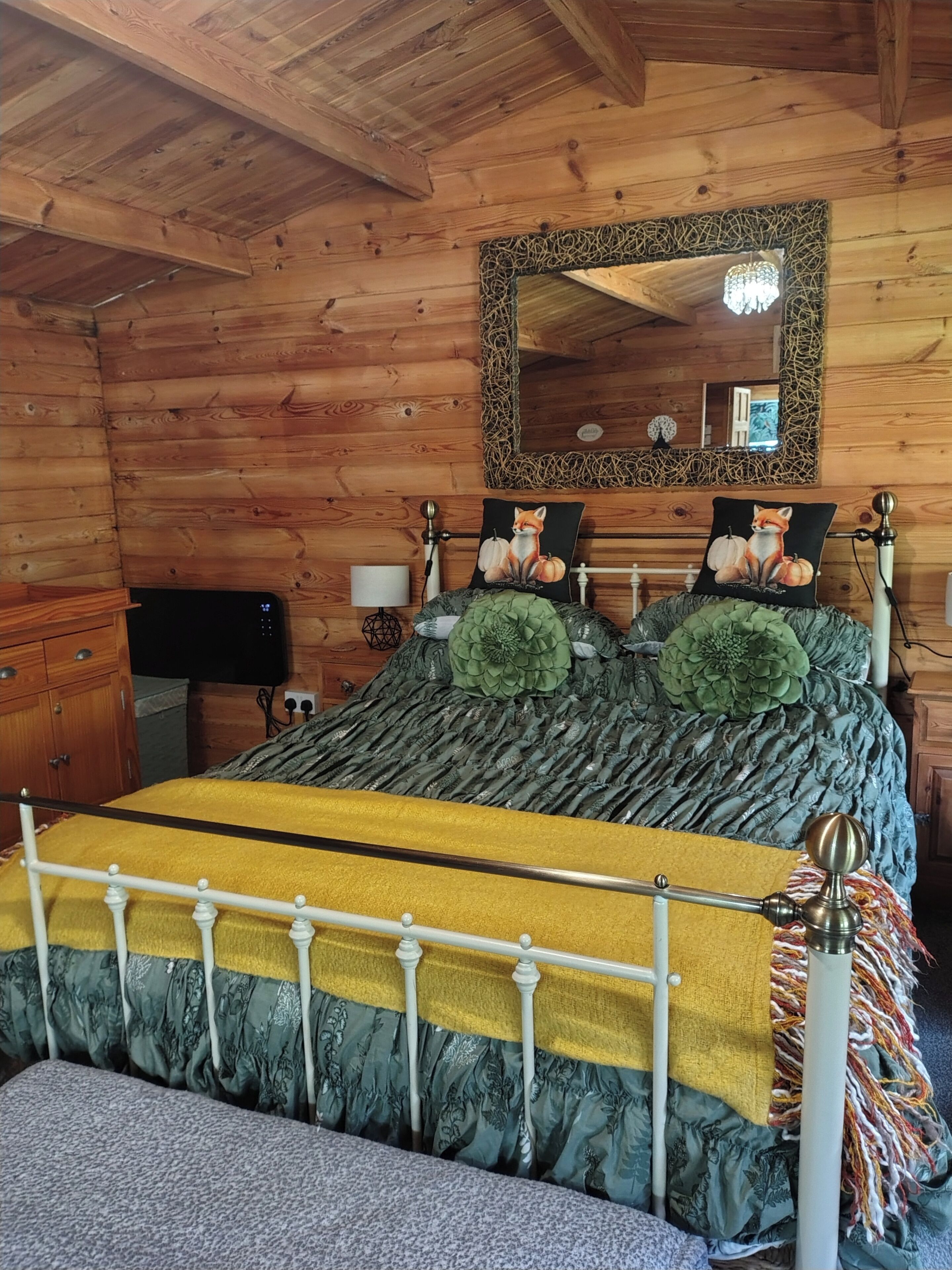 A wooden cabin bedroom with a bed, a mirror, and a dresser.