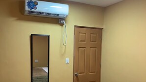 Une pièce comprenant un lit, un ventilateur de plafond, un appareil de climatisation, une porte et un miroir.