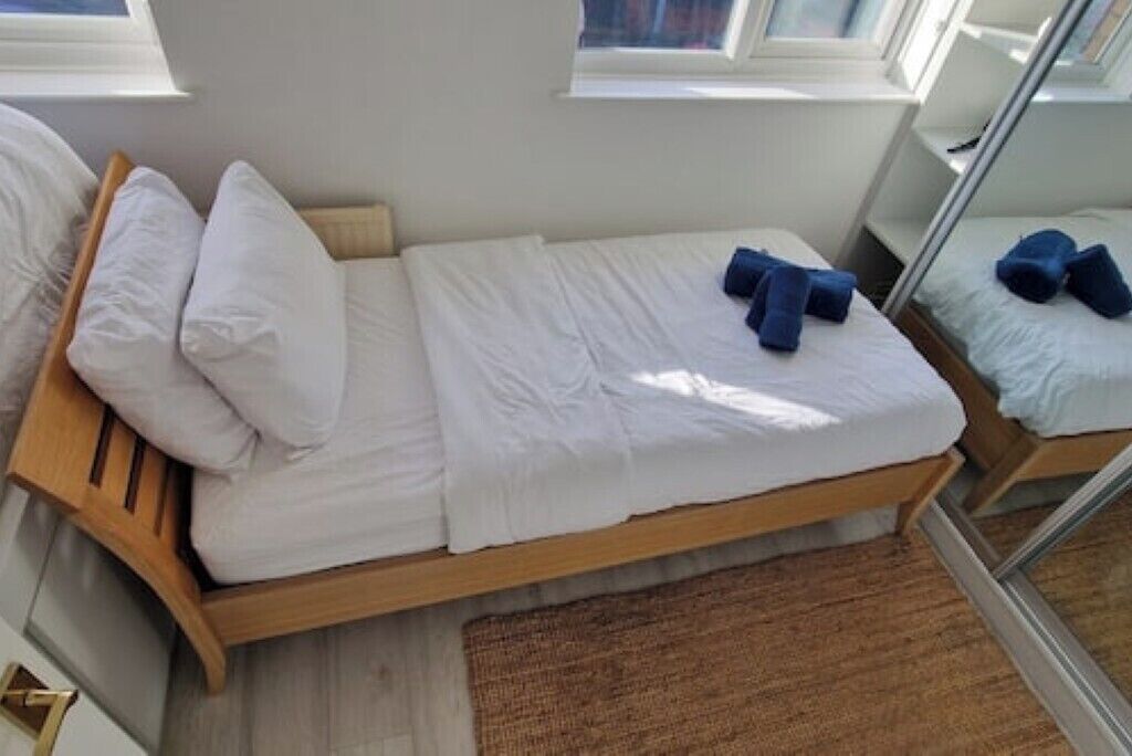 Een eenpersoonsbed met wit beddengoed en blauwe kussens, een houten hoofdbord en een raam met uitzicht.