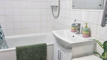 Une salle de bain avec une baignoire blanche, un lavabo et une douche. On trouve des articles de toilette sur le lavabo et une serviette est accrochée au mur.