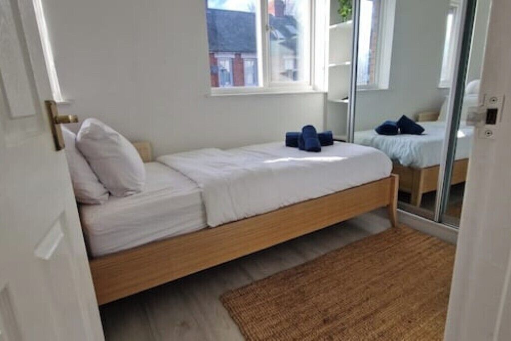 A small, single-bed room with a wooden frame, white bedding, and a brown rug.