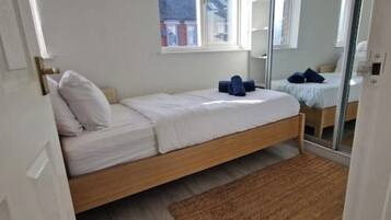 A small, single-bed room with a wooden frame, white bedding, and a brown rug.