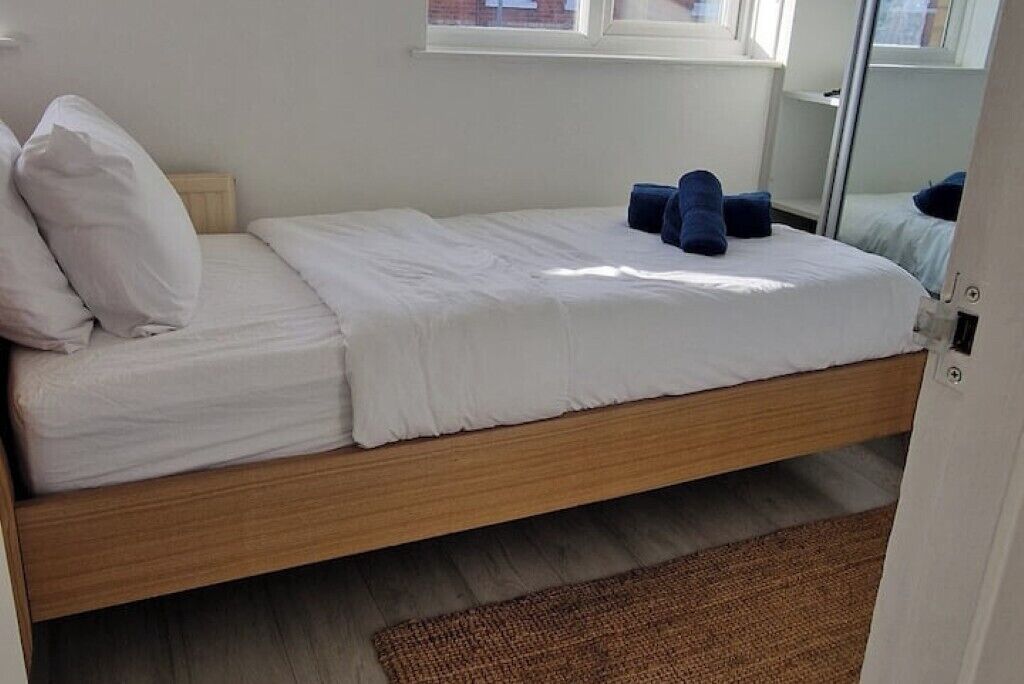 Een enkel bed met witte lakens, een houten frame en een bruin vloerkleed.