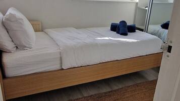 Een enkel bed met witte lakens, een houten frame en een bruin vloerkleed.