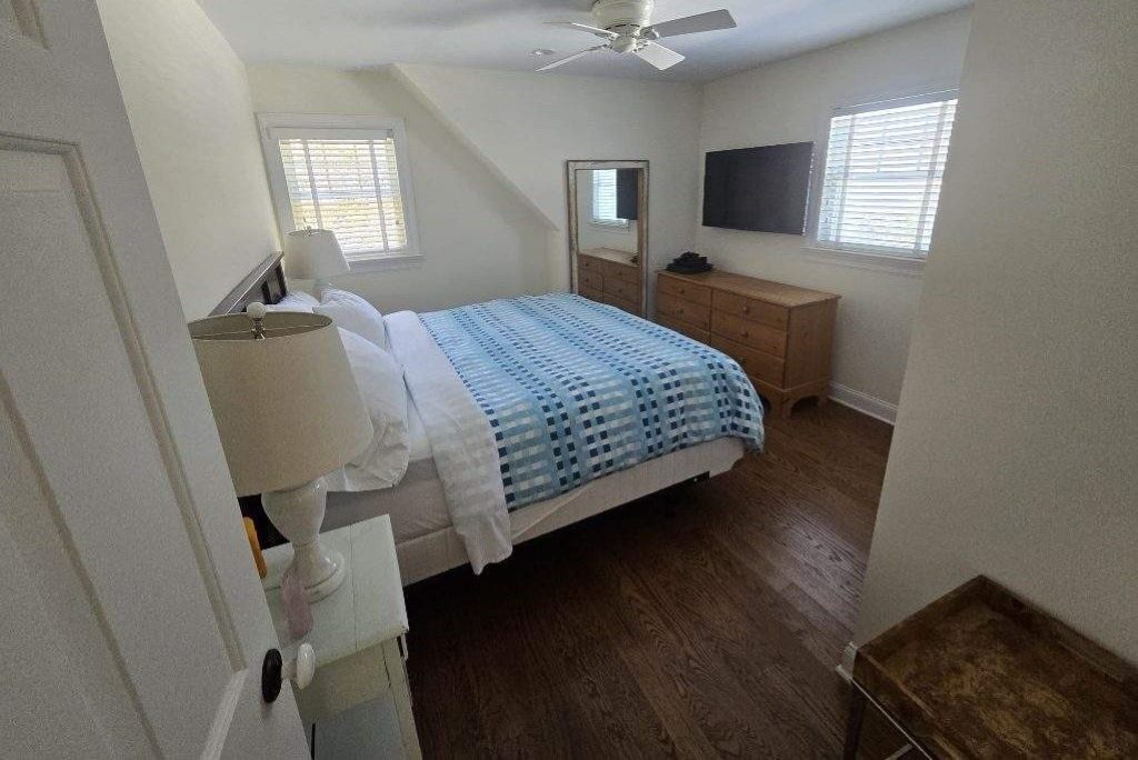 A bedroom with a bed, dresser, mirror, ceiling fan, and two windows.