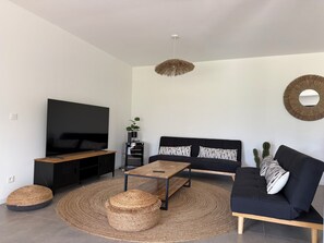 A modern living room with a flat-screen TV, black sofa, wooden coffee table, woven pouf, and a hanging light fixture. - Air-conditioned villa with views, swimming pool and outdoor entertainment area. (Figari)