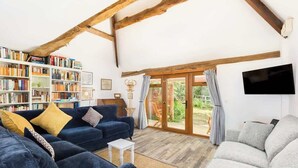 A cozy living room with a blue sofa, a grey armchair, and a bookshelf filled with books. - Rural, Self-Contained 1Bed, The Writer's Retreat (Hampton Lucy)