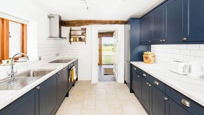 A modern kitchen with dark blue cabinets, white countertops, and a visible stove. There is a wooden door on the left and a view of the outdoors through an open doorway. - Rural, Self-Contained 1Bed, The Writer's Retreat (Hampton Lucy)