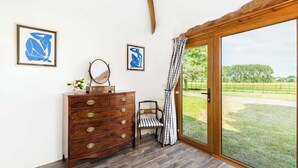 A room with a wooden dresser, a chair, and a large sliding glass door leading to a grassy outdoor area. - Rural, Self-Contained 1Bed, The Writer's Retreat (Hampton Lucy)