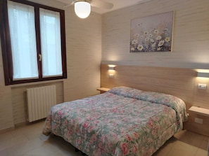 Une chambre à coucher avec un lit, une fenêtre avec des rideaux, un radiateur, un tableau accroché au mur et des lampes de chevet.