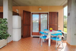 Un patio couvert comprenant une table et des chaises, un réfrigérateur et une porte donnant sur un jardin.