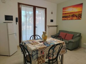 Un coin repas avec une table recouverte d’une nappe ornée d’une carte ancienne, un vase posé sur la table et, au fond, un canapé vert agrémenté de coussins rouges.