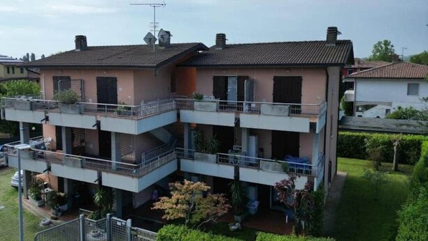 Ein mehrgeschossiges Wohngebäude mit Balkonen, einem eingezäunten Garten und blauem Himmel.
