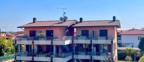 A multi-story residential building with balconies, a parking area, and a clear sky.
