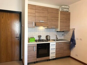 A compact kitchen with wooden cabinets, a gas stove, a dishwasher, and a sink. - Cornflower Apartment - First Floor (Sirmione)