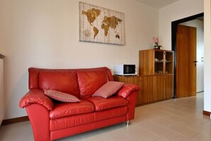 A red leather sofa with plaid cushions, a world map on the wall, a wooden cabinet with a microwave, and a door in the background. - Cornflower Apartment - First Floor (Sirmione)