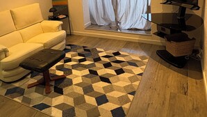 Una sala de estar con un sofá, una mesa de centro, un televisor y una alfombra estampada.