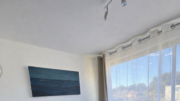 Un dormitorio con cama, un cuadro en la pared y una ventana con cortinas.