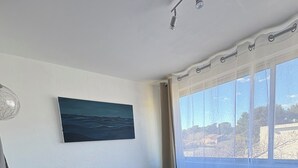 Una habitación con una cama, un cuadro, una ventana con cortinas y una lámpara en el techo.