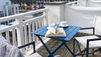 A blue table with a book and two cups on a deck with white railings.