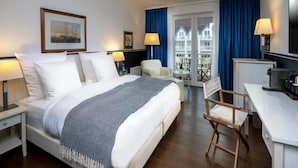 Quarto de hotel com cama, secretária, cadeira, televisão e varanda com cortinas azuis.