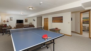 En rummelig stue med et pingpongbord, en sofa, et fjernsyn og et træskab.