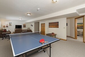Ein geräumiges Wohnzimmer mit Tischtennisplatte, einer Couch, einem Fernseher und einem Holzschrank.
