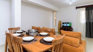 Un coin repas avec une table en bois dressée pour quatre personnes, entourée de chaises en bois. Un téléviseur est fixé au mur, à droite.