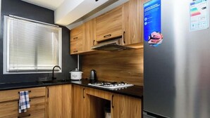 Une cuisine moderne avec des meubles en bois, un réfrigérateur en acier inoxydable, une cuisinière à gaz et une fenêtre équipée de stores.